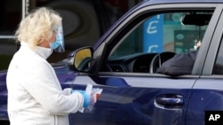 An Exam Corp. Lab employee, left, conducts a COVID-19 test at the parking lot of the facility in Niles, Ill., Oct. 21, 2020. 