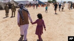 FILE - A man walks with a child through Fort Bliss' Doña Ana Village where Afghan refugees were being housed, in New Mexico, Sept. 10, 2021. 