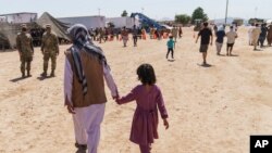 A man walks with a child through Fort Bliss' Doña Ana Village where Afghan refugees are being housed, in New Mexico, Friday, Sept. 10, 2021. The Biden administration provided the first public look inside the U.S. military base where Afghans…