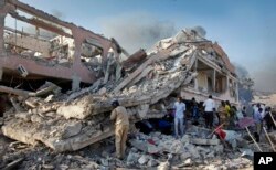 FILE - In this Oct 14, 2017, file photo, people gather to search for survivors by destroyed buildings at the scene of a blast in the capital Mogadishu, Somalia.