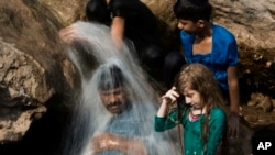 FILE - A family cools off in a stream during a heat wave, in Islamabad, Pakistan, May 30, 2017. The town of Turbat in southwestern Pakistan reported a temperature of 54 degrees Celsius in May.
