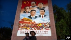 FILE - A man holds a girl in front of a large mural depicting Chinese President Xi Jinping and other Chinese leaders at a public square at the base of the Potala Palace in Lhasa in western China's Tibet Autonomous Region, June 1, 2021.