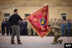 Ukrainian President Volodymyr Zelenskyy (L) holds a flag of the Ukrainian armed forces as a Ukrainian serviceman pays his respects during a ceremony marking Defenders Day of Ukraine in Kyiv on October 1, 2023. (Ukrainian Presidential Press Service/AFP)