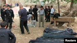 Các quan chức cảnh sát và chính phủ đứng gần thi thể các nạn nhân vụ đụng độ đẫm máu tại Tân Cương hồi tháng 4, 2013.