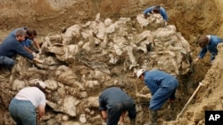 FILE - International war crimes tribunal investigators clear away soil and debris from dozens of Srebrenica victims buried in a mass grave near the village of Pilica, some 55 kms (32 miles) northeast of Tuzla, in 2006.