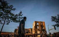 A man walks on Lake Street while looking at businesses destroyed during riots and protests over the death of George Floyd, May 31, 2020, in Minneapolis.