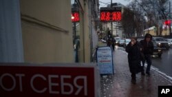 People walk along the Boulevard Ring in downtown Moscow, Russia, Wednesday, Dec. 24, 2014 with a currency exchange office sign on a wall. 