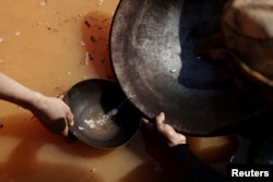 Miners rub mercury that has coagulated into tiny particles of gold in a basin at a mine near Crepurizao, Brazil, Aug. 5, 2017.