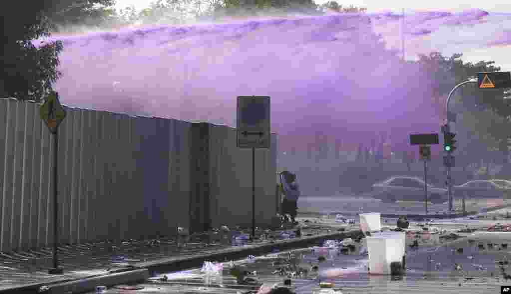 A man shields himself as riot police shoot water cannon at anti-government protesters at a gymnasium in Bangkok, Dec. 26, 2013. 