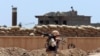 FILE - A Kurdish peshmerga fighter carries his weapon as he walks to his base where two Islamic State flags are seen on a building, right, and a water tower, left, south of Kirkuk, northern Iraq, June 25, 2014. 
