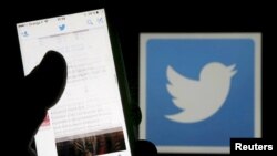 FILE - A man reads tweets on his phone in front of a displayed Twitter logo in Bordeaux, southwestern France, March 10, 2016. 