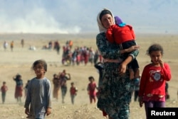 FILE - Displaced Yazidis, fleeing violence from forces loyal to the Islamic State group, head toward the Syrian border Aug. 11, 2014.