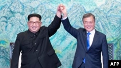 Pemimpin Korea Utara Kim Jong-un (kiri) dan Presiden Korea Selatan Moon Jae-in (kanan) mengangkat tangan mereka yang bergandengan, dalam upacara penandatanganan kesepakatan menjelang berakhirnya pertemuan bersejarah mereka di desa gencatan senjata Panmunjom, 27 April 2018. 