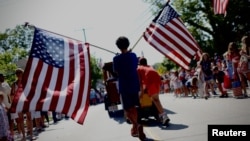 A boy carries American flags through Barnstable Village, Massachusetts, on Cape Cod during the annual Fourth of July Parade celebrating the country's Independence Day on July 4, 2024.