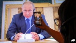 A journalists watches a TV broadcast showing Russian President Vladimir Putin at the St. Petersburg International Economic Forum, in St. Petersburg, Russia, June 6, 2019.
