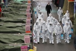 Workers wearing protective gear spray disinfectant at a market in the southeastern city of Daegu, South Korea, as a preventive measure after the COVID-19 coronavirus outbreak, Feb. 23, 2020.