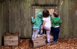 FILE - Children peer out a screened window in the fence at a child care center in Seattle, Aug. 27, 2018.
