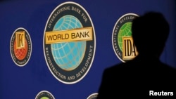 FILE - A man is silhouetted against the logo of the World Bank at the main venue for the International Monetary Fund (IMF) and World Bank annual meeting in Tokyo on October 10, 2012. The World Bank Group plans to invest more of its funds to help developing countries adapt to the impacts of climate change, in an effort to stop extreme weather and rising seas from making poverty worse.