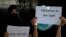 FILE - Afghan girls hold illegal protest signs to demand the right to education, in a private home in Kabul, Afghanistan, on Aug. 2, 2022.