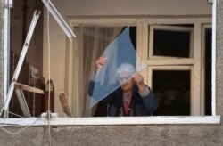 An elderly woman throws a piece of glass from her balcony in an apartment building damaged by shelling by Azerbaijan's artillery during a military conflict in Stepanakert, the separatist region of Nagorno-Karabakh, Oct. 12, 2020.