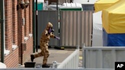 A specialist team member in a military protective walks away after standing in a foot bath as they leave the front entrance of John Baker House for homeless people on Rollestone Street in Salisbury, England, Friday, July 6, 2018. 