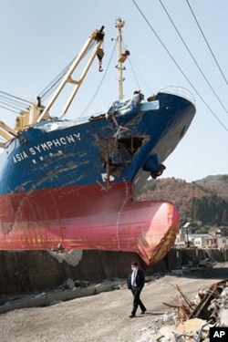 A man walks past a huge ship that breached a seawall in Kamaichi, Japan