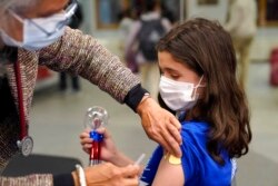 Jehna Kottori, 10, of Worcester, Mass., right, prepares to receive a shot of Pfizer COVID-19 vaccine, Dec. 2, 2021, at a mobile vaccination clinic, in Worcester.