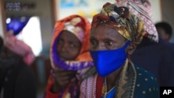 FILE - A woman waits for the AstraZeneca coronavirus vaccine at the Butanda Health Center III in Western Uganda, April 27, 2021.
