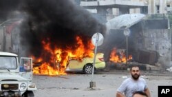 In this photo released by the Syrian official news agency SANA, Syrians gather in front of a burning car at the scene where suicide bombers blew themselves up, in the coastal town of Tartus, Syria, Monday, May 23, 2016.