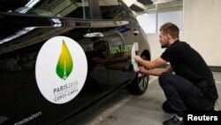 FILE - An employee installs a sticker which reads 100% electric next to the logo of the upcoming COP21 Climate Change Conference on a Nissan LEAF electric car in Boulogne-Billancourt, near Paris, France, November 16, 2015.