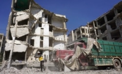 A member of the Syrian Civil Defense, also known as the White Helmets, stands in front of a heavily damaged building following an airstrike by regime forces in the rebel-held city of Idlib in northwestern Syria, July 12, 2019.