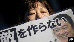 Seorang perempuan memegang poster bertuliskan: "Jangan mencari musuh" dan membawa fotonya di depan kediaman resmi perdana menteri di Tokyo, 1 Februari 2015.