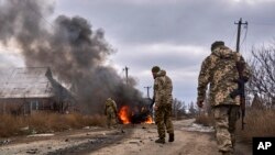 Tentara Ukraina melewati bus sukarelawan yang terbakar setelah drone Rusia menabraknya di dekat Bakhmut, wilayah Donetsk, Ukraina, Kamis, 23 November 2023. (Foto: via AP)