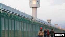 FILE - Workers walk by the perimeter fence of what is officially known as a vocational skills education centre in Dabancheng in Xinjiang Uighur Autonomous Region, China, Sept. 4, 2018. 