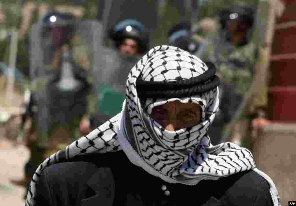 An elderly Palestinian man walks past Israeli soldiers deployed at the entrance of the al-Aroub Palestinian refugee camp, just north the West Bank town of Hebron, May 15, 2012.