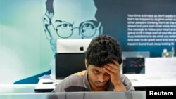 FILE - An employee works on a computer terminal against the backdrop of a picture of late Apple co-founder Steve Jobs at the Start-up Village in Kinfra High Tech Park in the southern Indian city of Kochi.