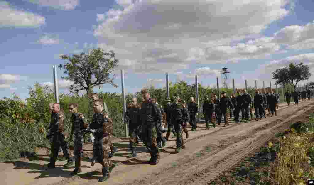 Hungarian soldiers walk past a razor wire fence that is being built along the border with Croatia near the village of Sarok. Prime Minister Viktor Orban said that millions of migrants are &quot;laying siege&quot; to the borders of his country and of Europe, putting the continent in danger. &nbsp;