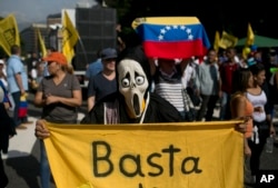 FILE - A protester, wearing a Ghostface mask and holding a banner that reads in Spanish, "Stop," takes part in a protest against President Nicolas Maduro, in Caracas, Venezuela, Oct. 26, 2016.