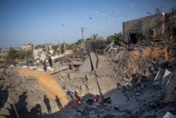 FILE - Palestinians sit amid the rubble of their destroyed house following overnight Israeli missile strikes, in the town of Khan Younis, southern Gaza Strip, Nov. 14, 2019.