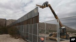 FILE - Workers raise a taller fence along the Mexico-US border between the towns of Anapra, Mexico and Sunland Park, New Mexico, Nov. 10, 2016. For almost two decades, a Mass has been celebrated there on the Day of the Dead to remember migrants who have 