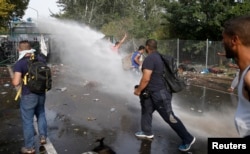 Migrants protest as Hungarian riot police fires tear gas and water cannon on the Serbian side of the border, near Roszke, Hungary Sept. 16, 2015.