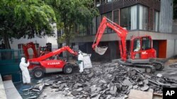 Workers direct a mechanical shovel grabbing pieces of destroyed surfacing to gather up the lead particles in the school yard of Saint Benoit primary school in Paris, France, Aug. 8, 2019.