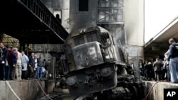 People look at a damaged train inside Ramsis train station in Cairo, Egypt, Wednesday, Feb. 27, 2019. The high-speed crash caused an explosion of the locomotive's fuel tank and triggered a huge blaze that engulfed that part of the station.