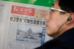 A man stands in front of a copy of the Global Times newspaper featuring an image of the U.S. Capitol during preparation for the inauguration of Joe Biden as the U.S. president, which is placed on a public display window in Beijing, Jan. 21, 2021.