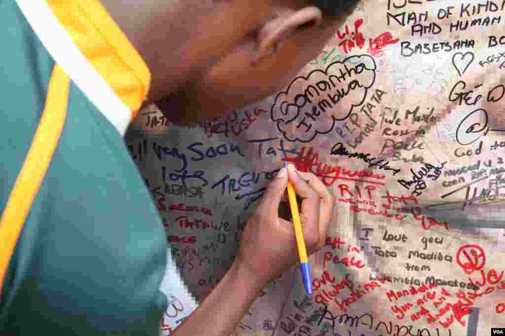 A young boy tried to squeeze his name onto a Mandela poster outside his home in Soweto, South Africa. (Hannah McNeish for VOA)