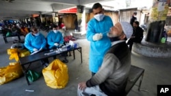 FILE - A health worker collects a swab sample from a man to test for COVID-19 in Jammu, India, Jan. 29, 2022.