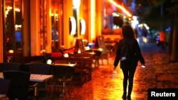 FILE - A woman passes empty tables before the late-night curfew due to restrictions against the spread of COVID-19 takes effect, in Berlin, Germany, Oct. 14, 2020.