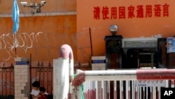 In this Aug. 31, 2018, file photo, children play outside the entrance to a school ringed with barbed wire, barricades and surveillance cameras near a sign which reads: "Please use the nation's common language" indicating the use of Mandarin in Peyzawat, w
