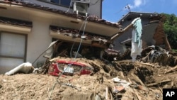 A car is covered with mud as houses are damaged after a mudslide caused by heavy rains in Hiroshima, southwestern Japan, July 10, 2018.