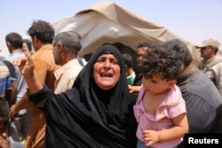 FILE - A women who fled Ramadi holds a child in a camp in the town of Amiriyat al-Fallujah, west of Baghdad, Iraq, May 22, 2015.